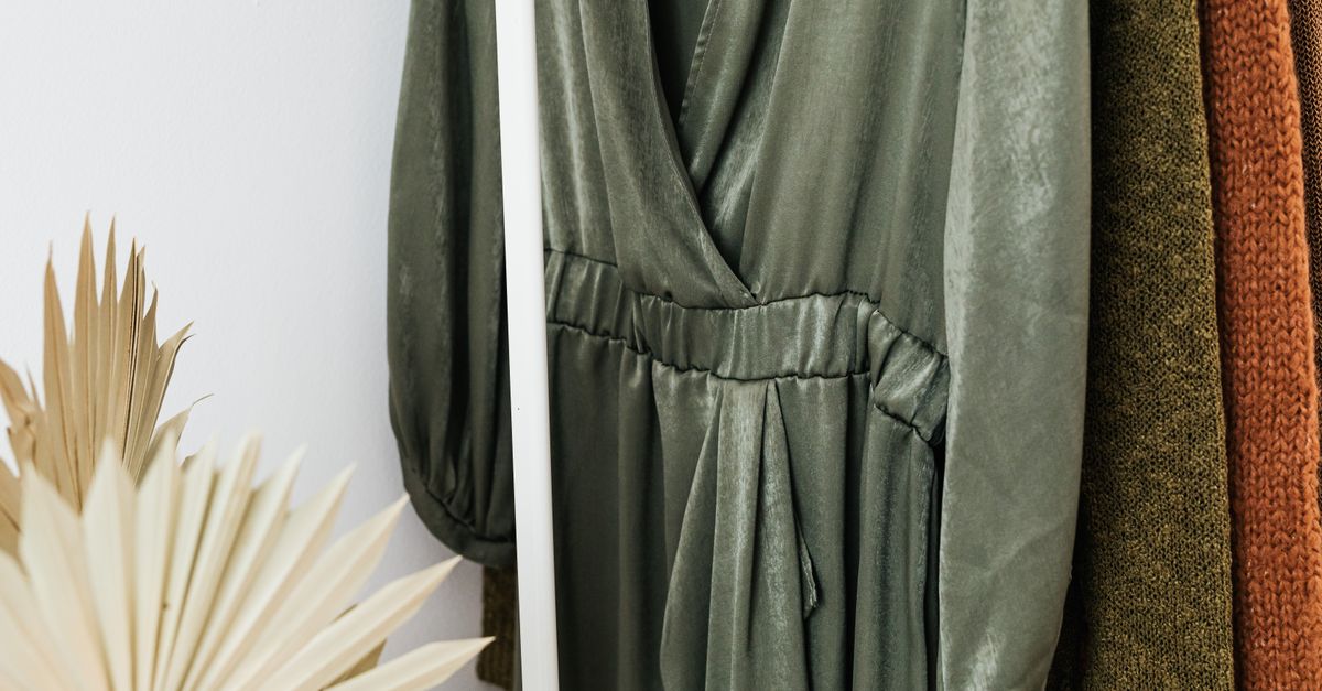 Stylish green dress on a clothes rack with knitted sweaters and dried leaves in a cozy setting.